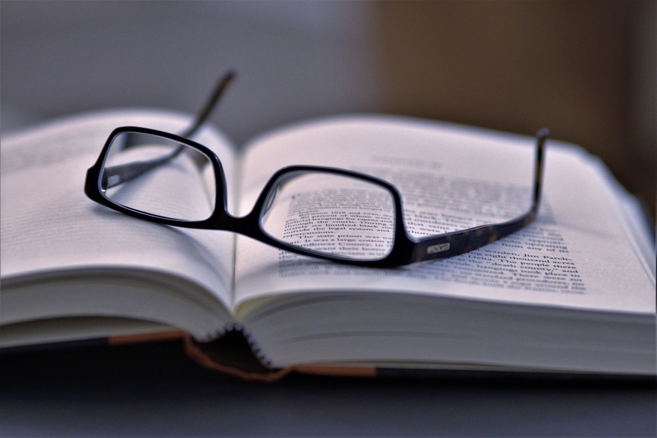 hero-img-01 Close-up of eyeglasses resting on an open book, highlighting reading and literature.