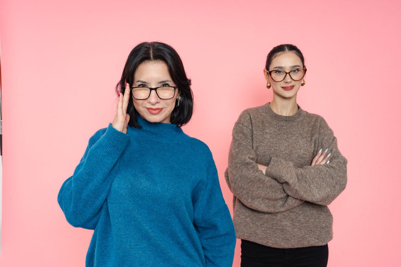 hero-img-02 Two stylish women wearing glasses pose confidently against a pink background.